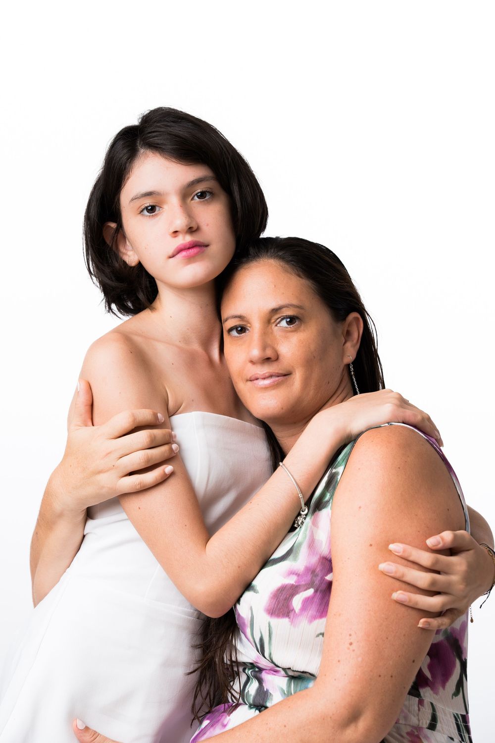 Two people embracing in a tender moment against white background, one wearing white dress and other in floral print top.