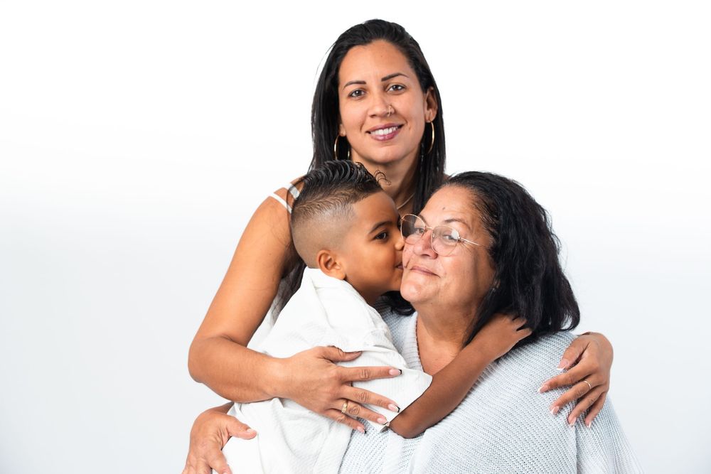 Multi-generational family embraces warmly against white background in studio portrait session.