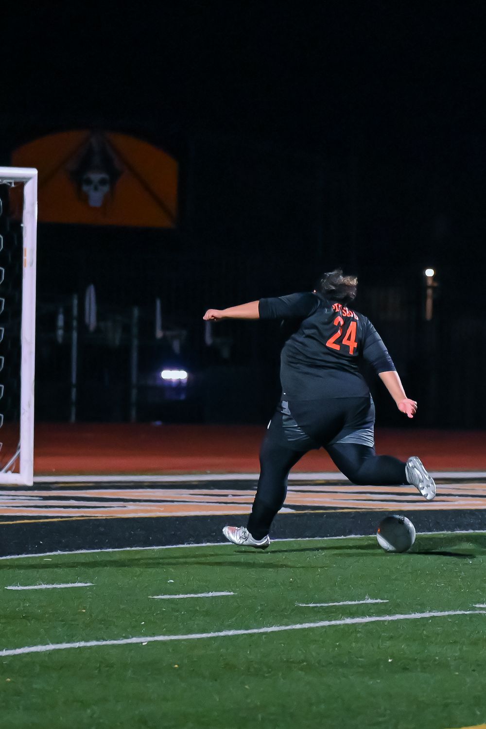 Soccer player in black uniform with number 24 slides across the field during nighttime game.