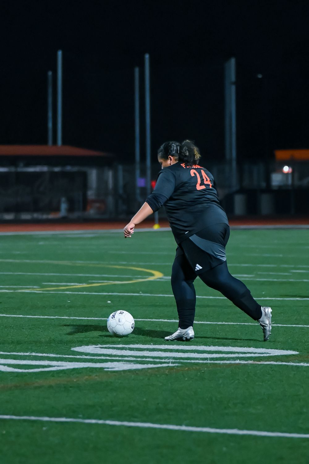 Soccer player in dark jersey makes a sliding tackle towards a white ball on the illuminated field.