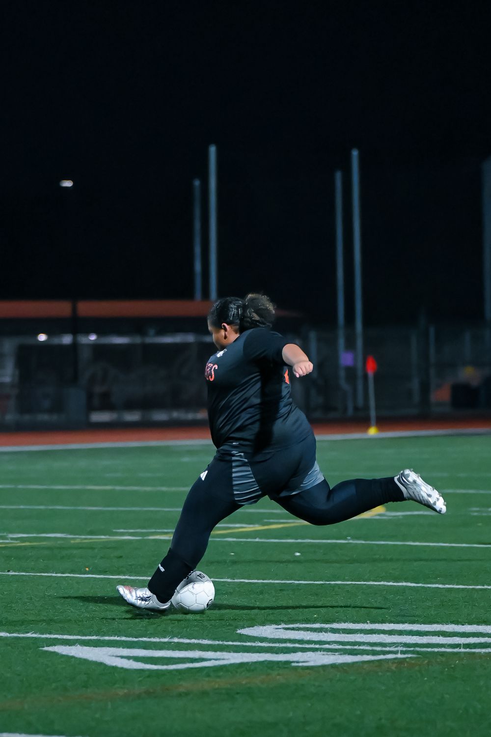 Player executes a diving save on the soccer field under stadium lights.