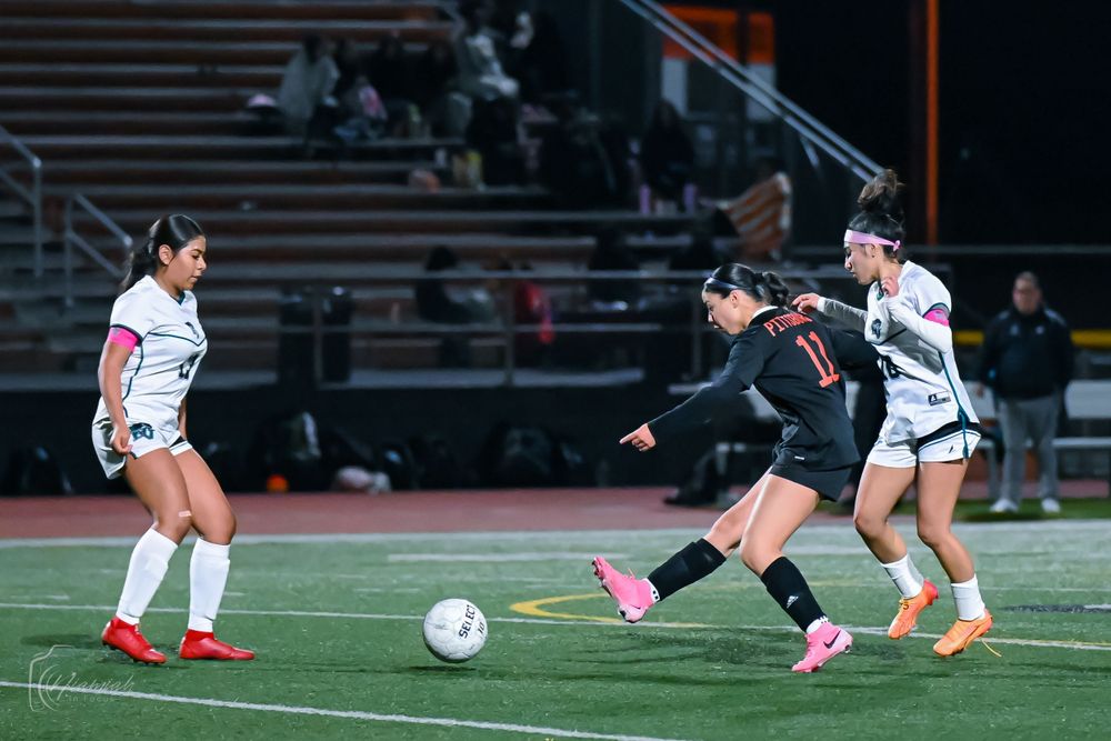 Soccer players slide across the field in pursuit of the ball during competitive night game.