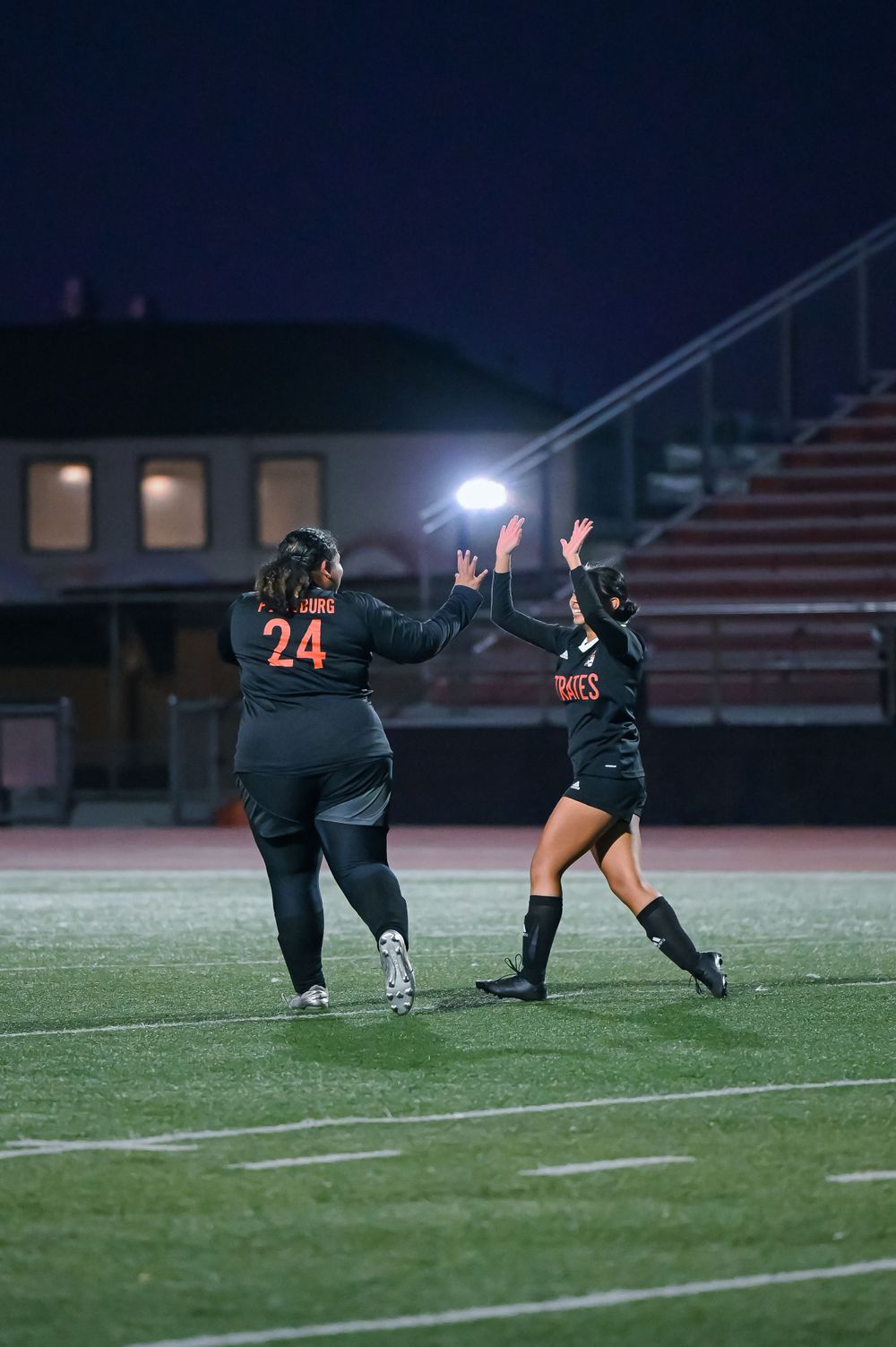Multiple players in black uniforms dive simultaneously on the soccer field during nighttime play.