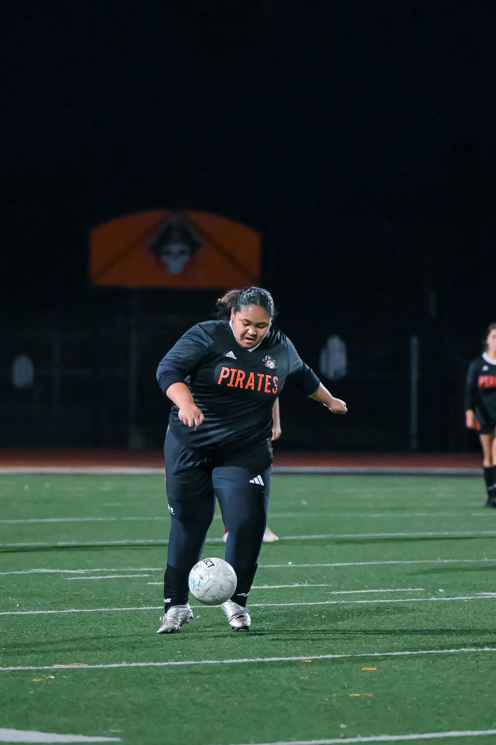 Soccer player in Pirates jersey attempts to control the ball on an illuminated field at night.