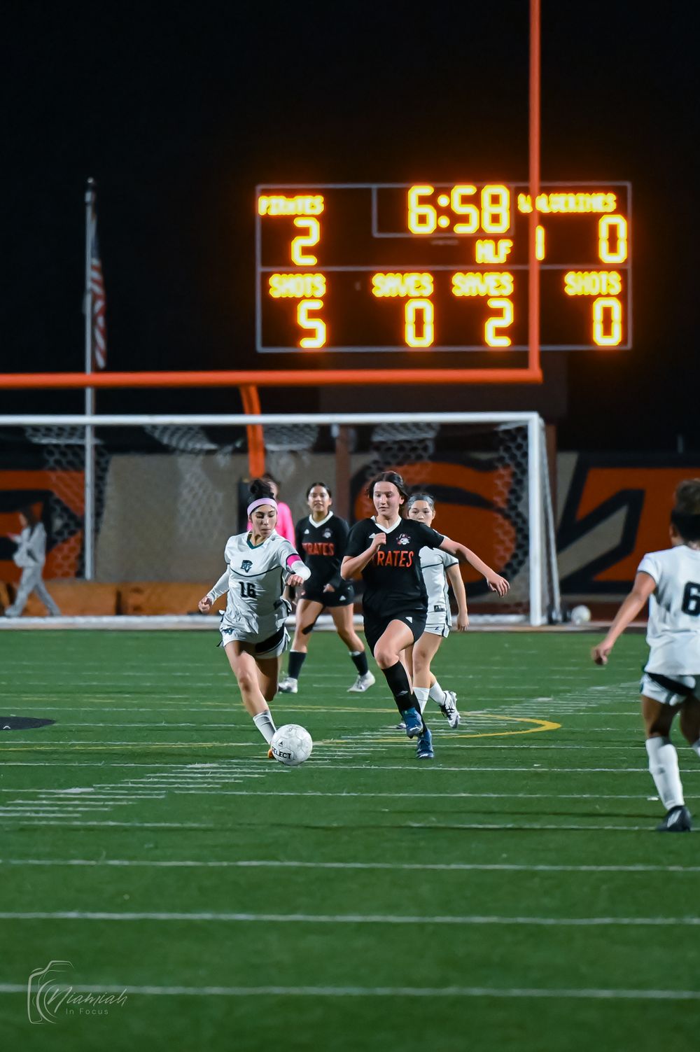 Soccer match action shot showing players competing with scoreboard displaying 6:58 in background.