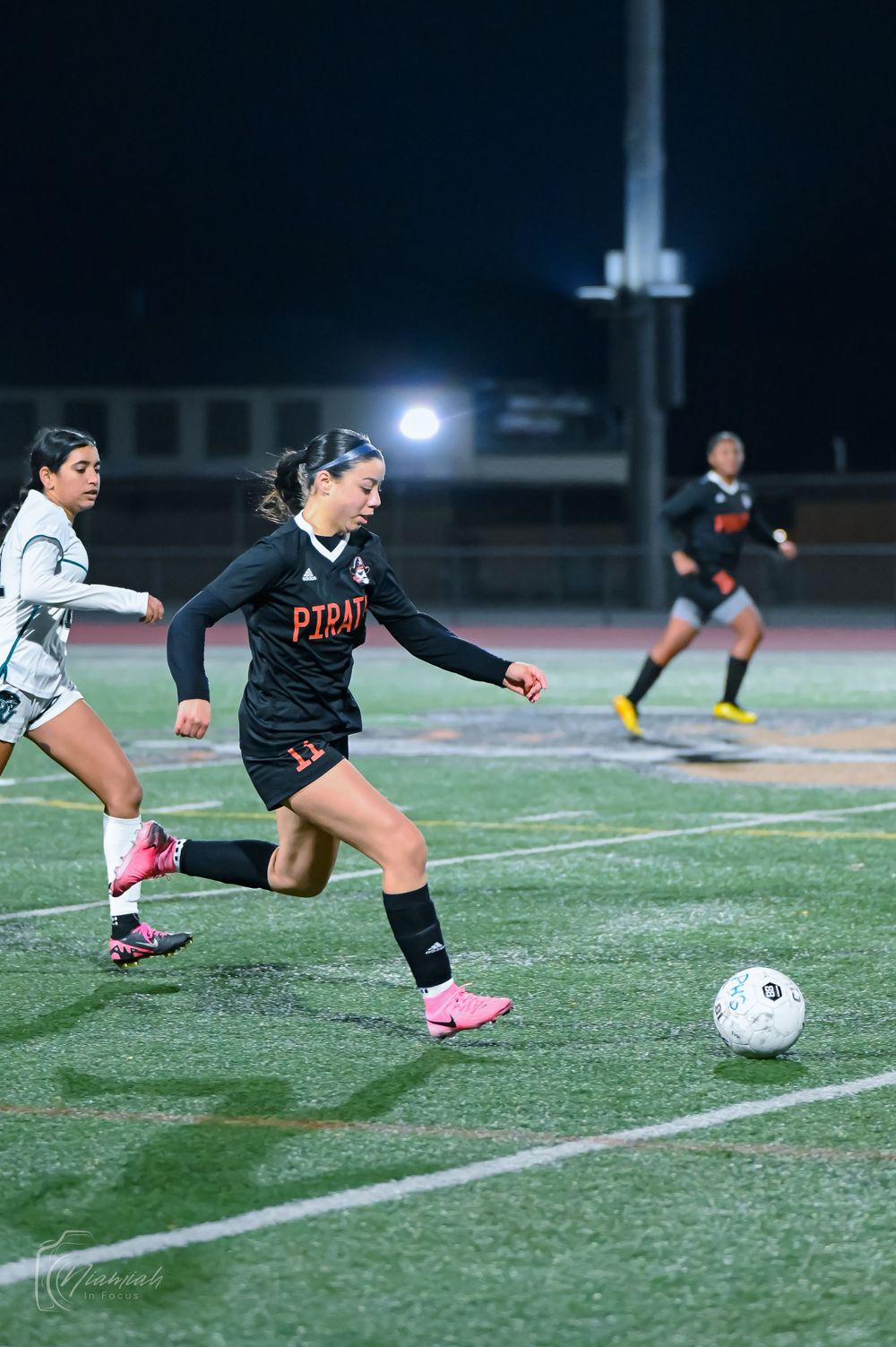 Soccer player in black uniform dribbles ball down field during nighttime match.