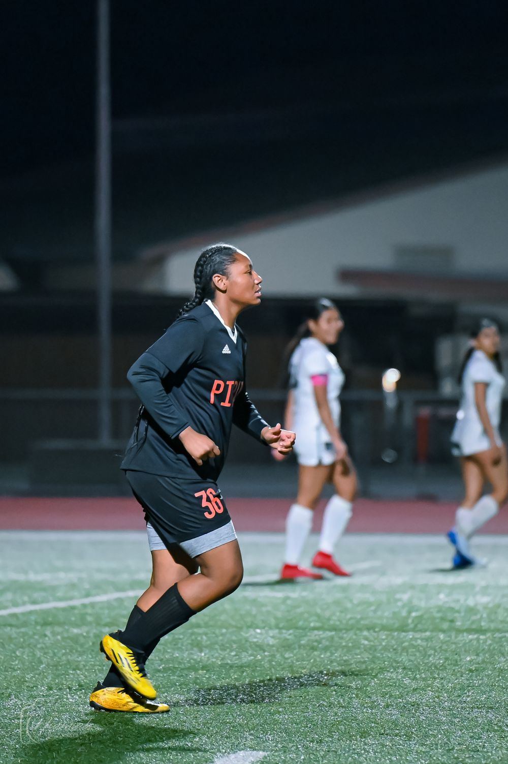 Player in black uniform runs across soccer field during evening game.