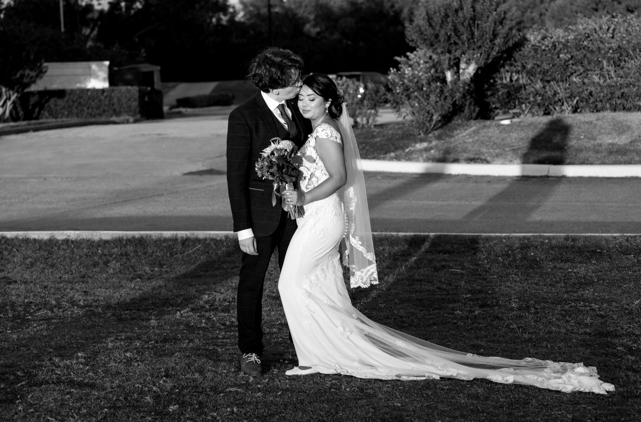 A romantic black and white wedding portrait of a couple embracing on a grassy lawn during their outdoor ceremony.