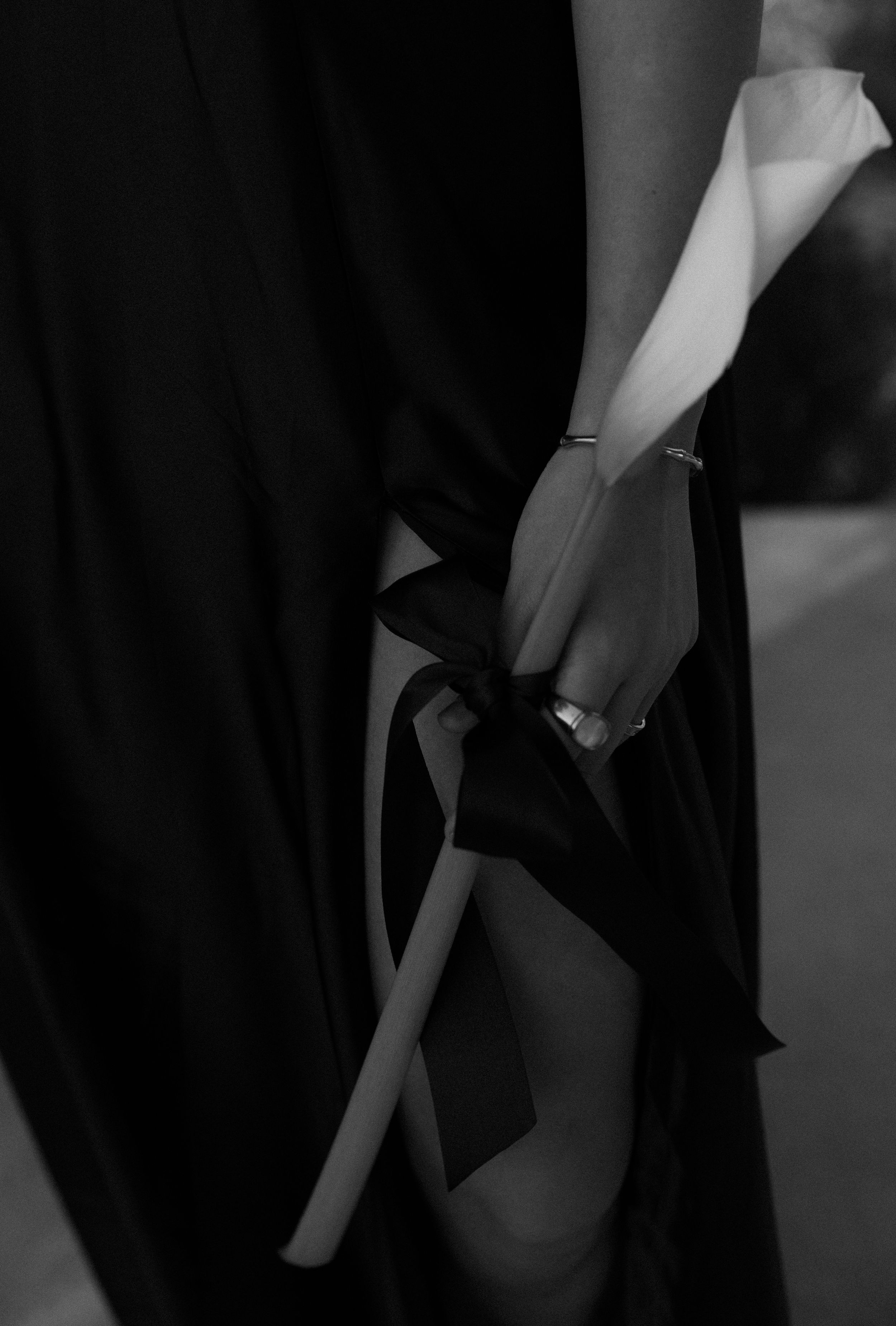 A black and white image shows a gloved hand elegantly holding a bow against dark fabric.