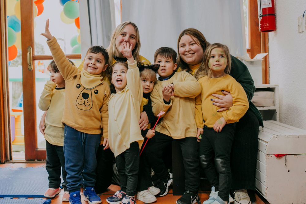 A group wearing coordinated yellow outfits pose together against a white wall decorated with orange balloons.