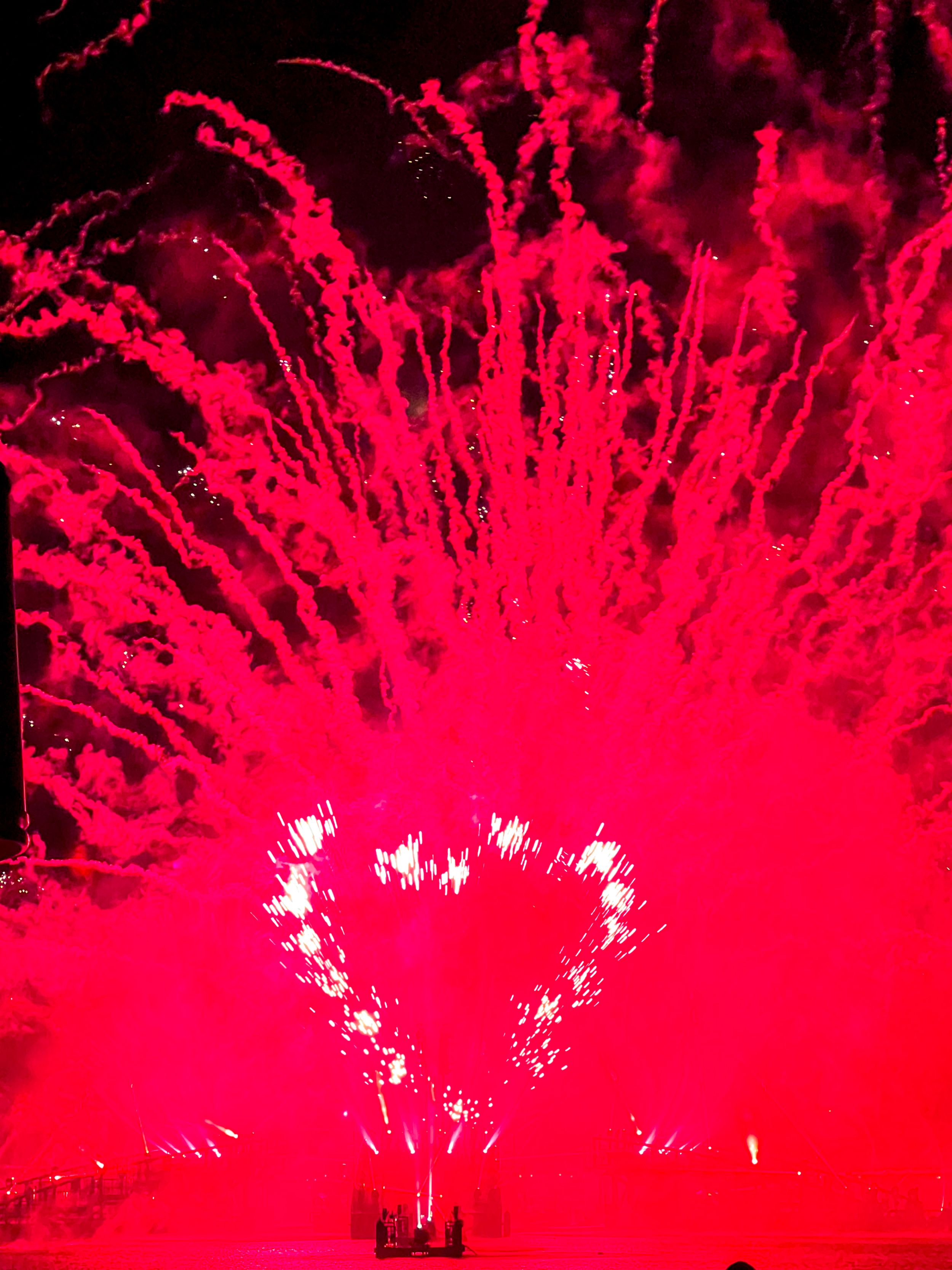 Red fireworks burst into a heart shape against dark night sky during celebration display.