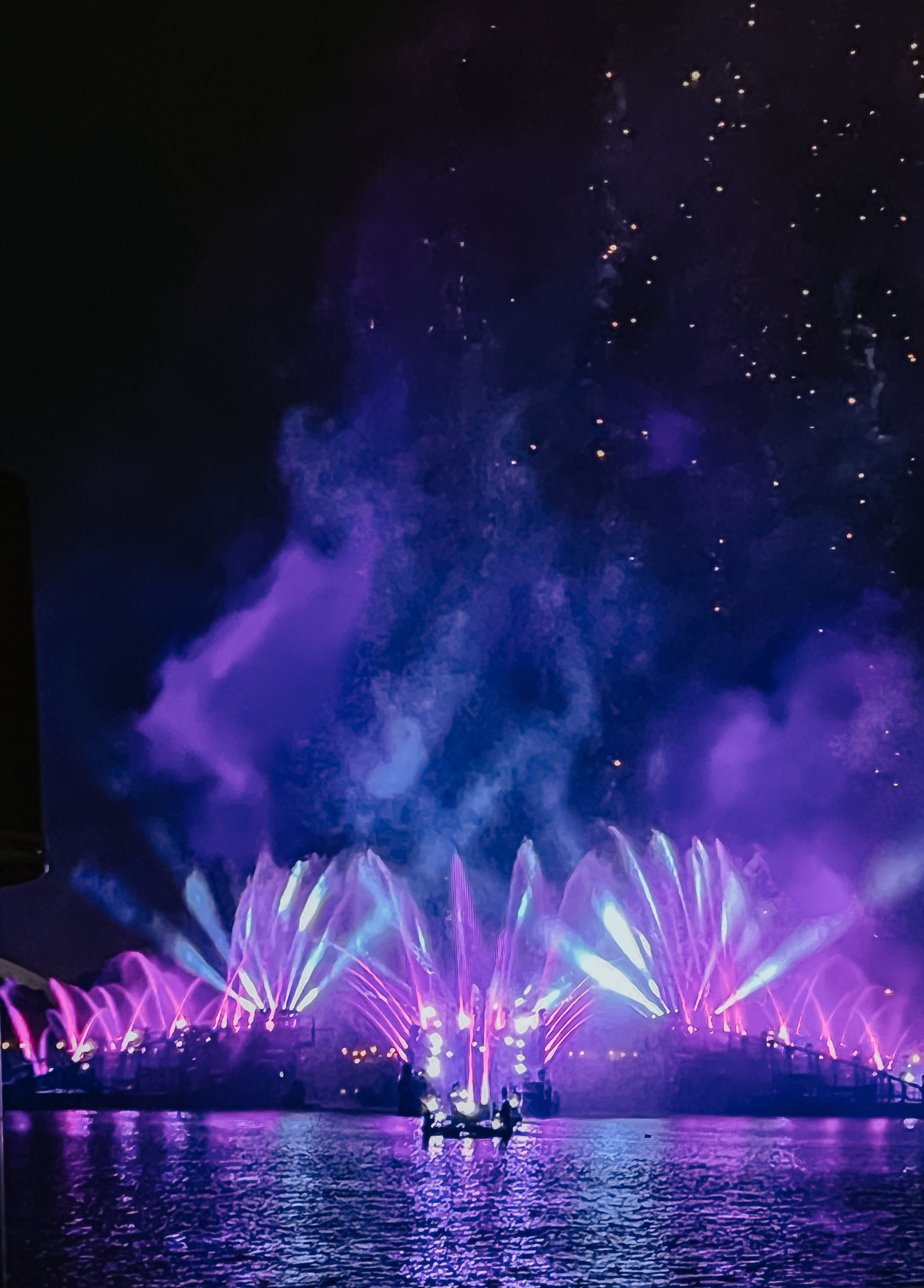 Spectacular night show with vibrant purple and blue fountain displays reflecting on water beneath a starry sky.