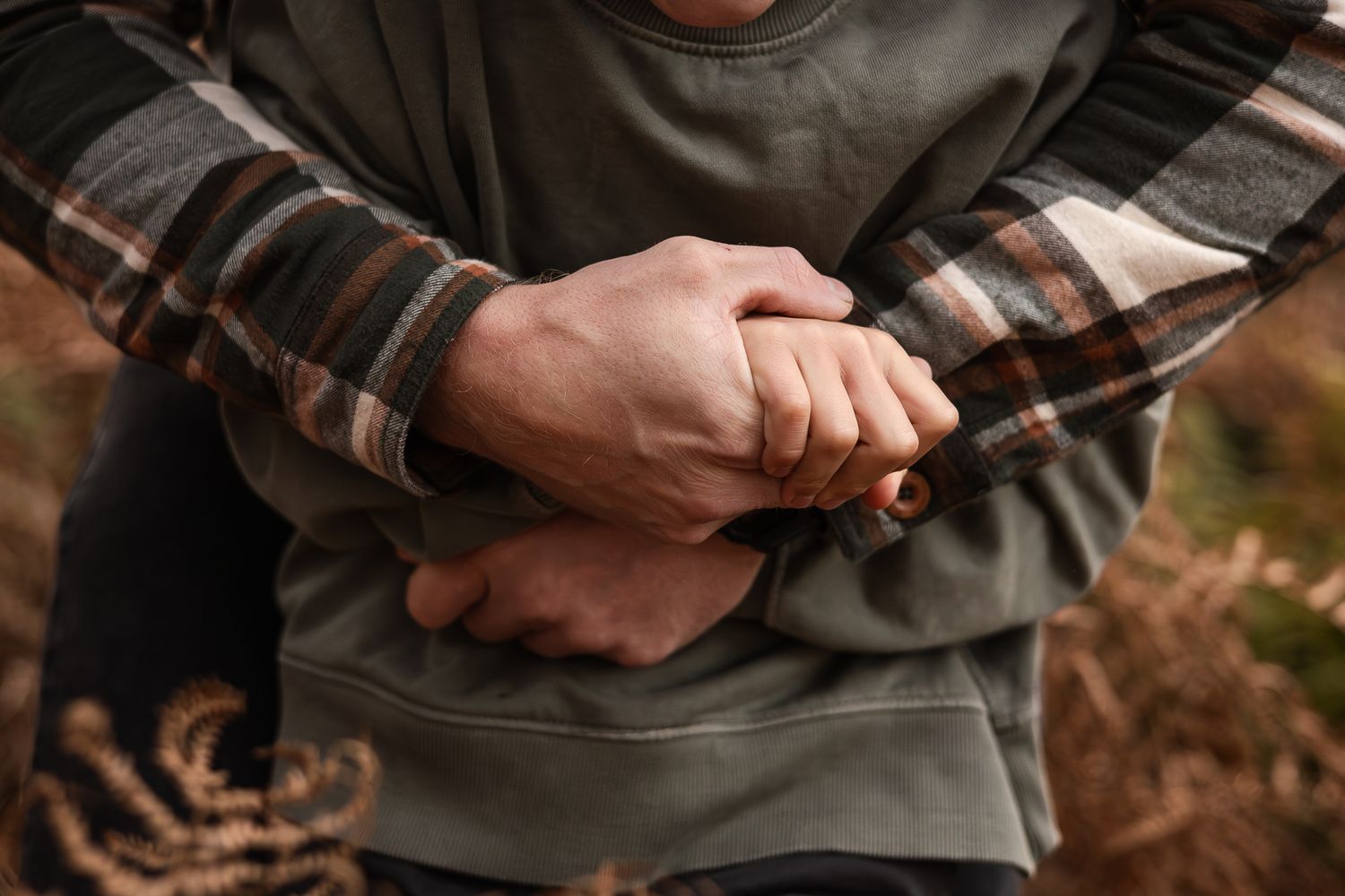 Close-up detail of hands holding plaid shirt sleeves in outdoor setting.