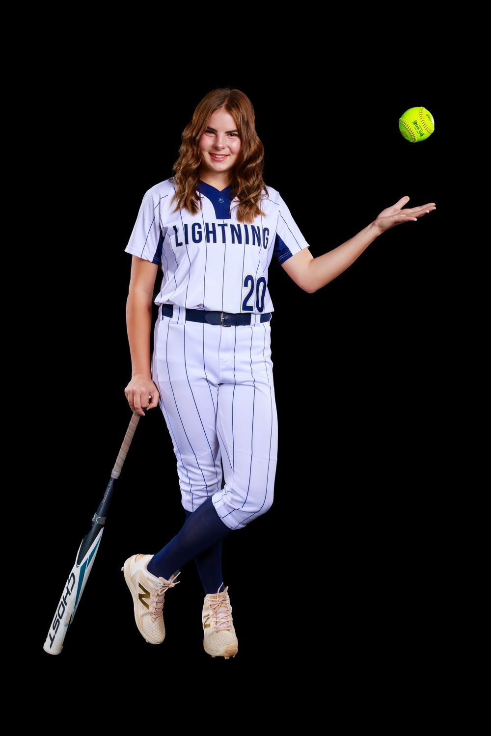 Softball player in white Lightning uniform with pinstripes poses with bat and ball against black background.