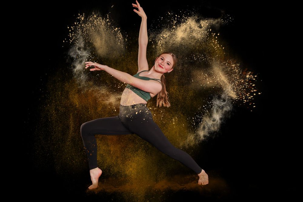 Dancer leaps gracefully through swirling gold powder creating dynamic motion art against black background.