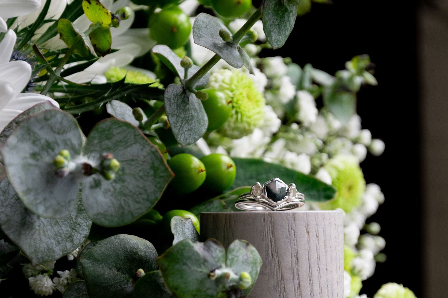 A delicate arrangement of green eucalyptus leaves and white baby's breath flowers frames a small gray decorative vase.