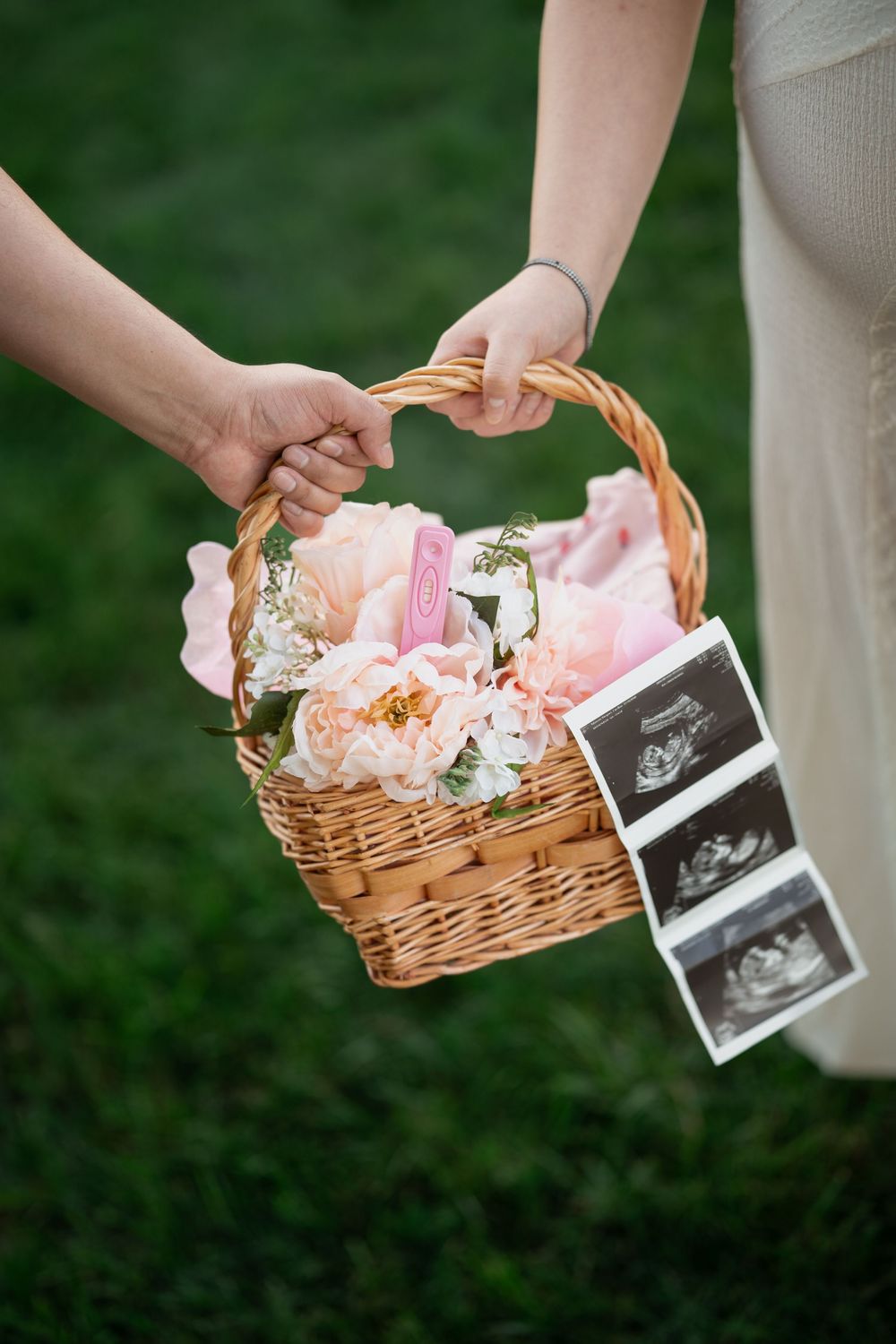 A wicker basket with pink flowers and ultrasound photos set up for a pregnancy announcement shoot.