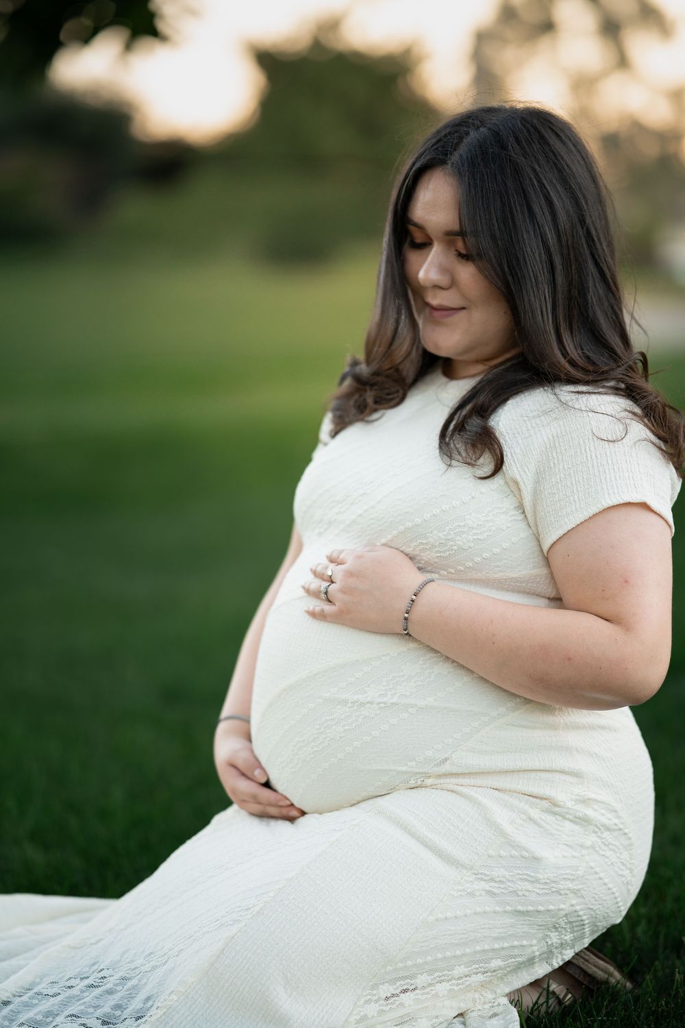 A maternity portrait series showing a woman in white dress cradling her baby bump in a park.