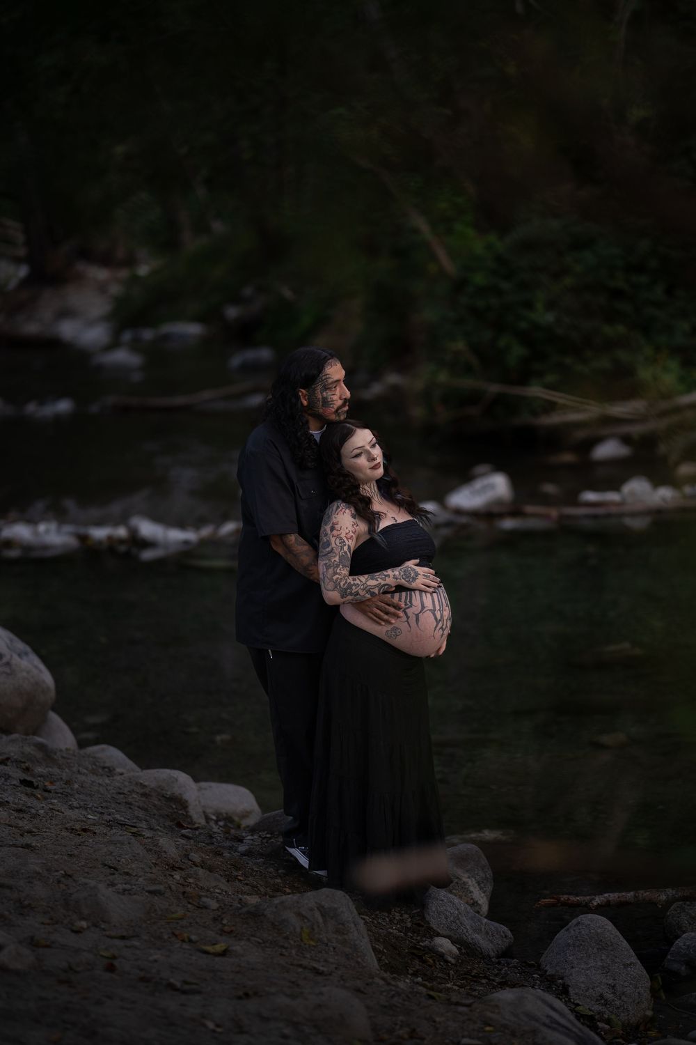 Romantic maternity photoshoot by riverside in moody dark setting.