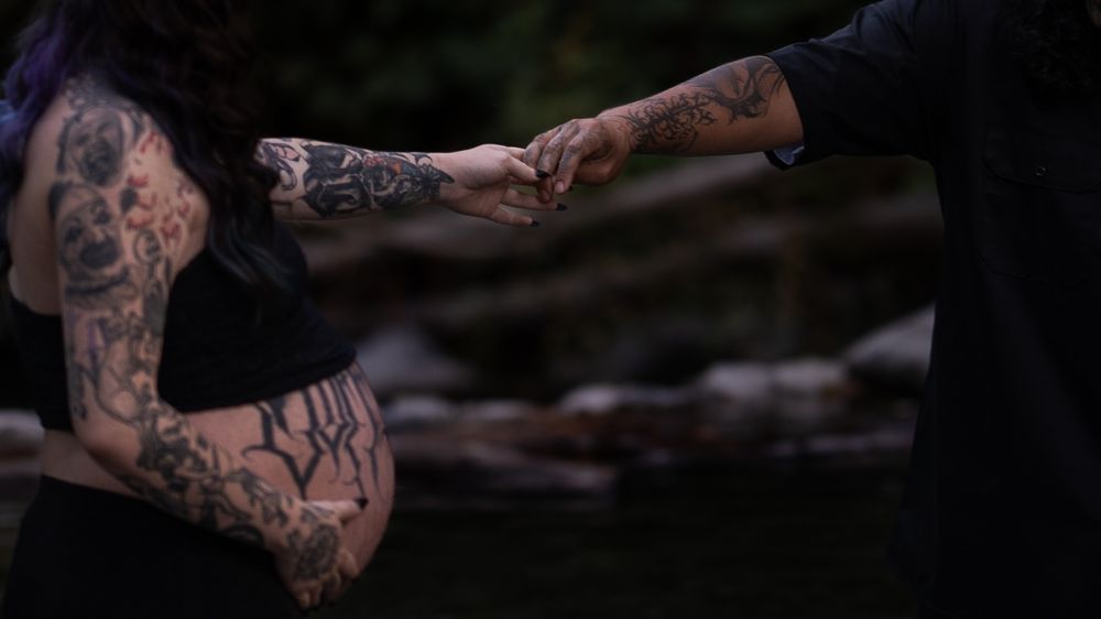 Artistic maternity photography session showcasing tattoo art in natural setting.