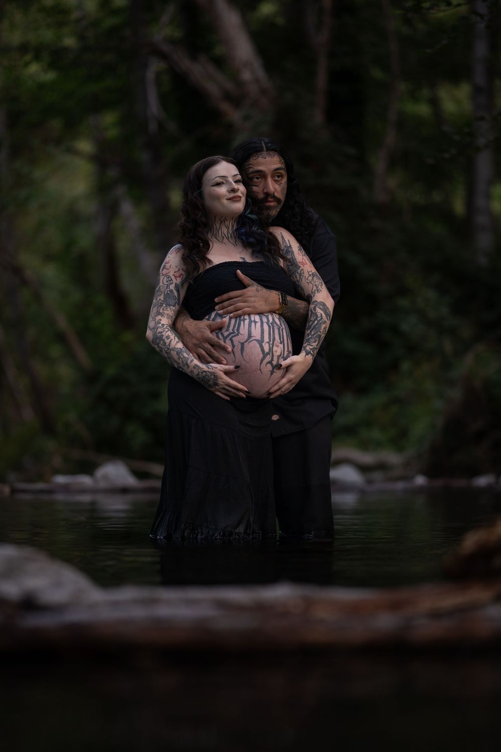 Atmospheric maternity photo session by a lake showing silhouettes embracing in moody lighting.