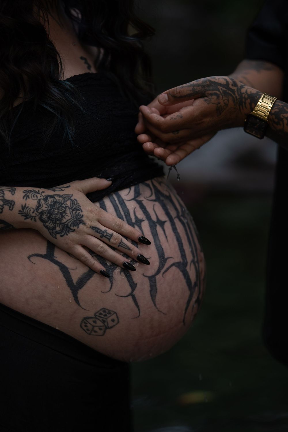 Artistic black and white photo focusing on detailed tattoos and hands on pregnant belly.