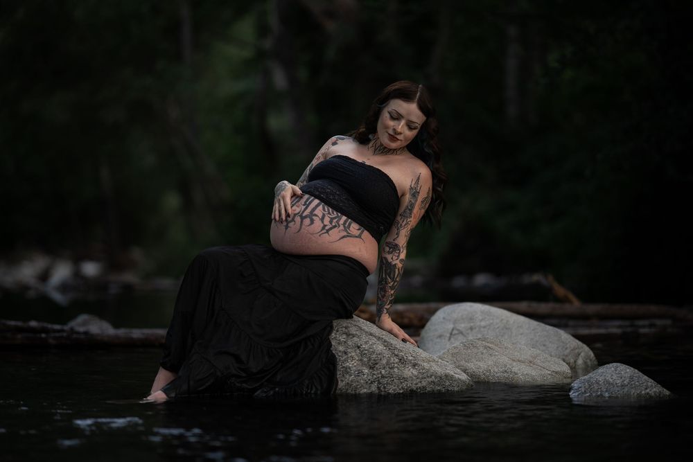 Artistic pregnancy photos taken at twilight near rocky waterfront.