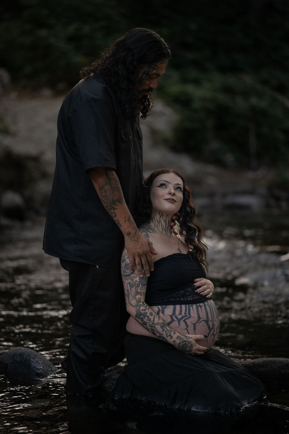 Intimate maternity portrait session captured in dark, atmospheric setting by water.