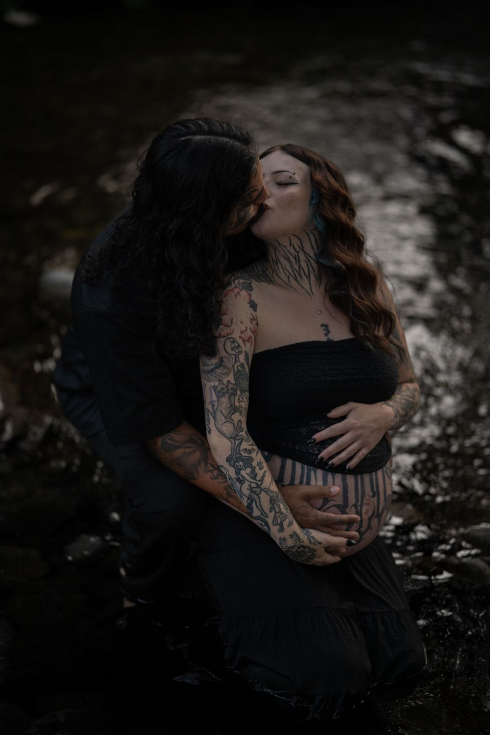 Romantic maternity photography with dramatic lighting and natural water backdrop.