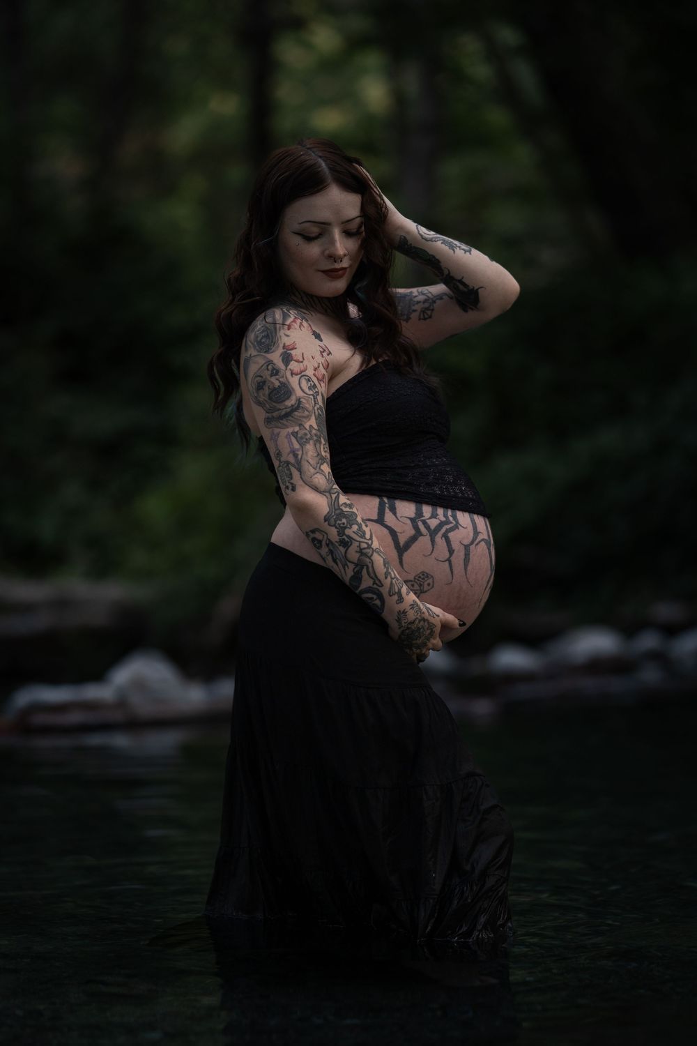 Artistic maternity photos featuring black dress and tattoos in nature setting.