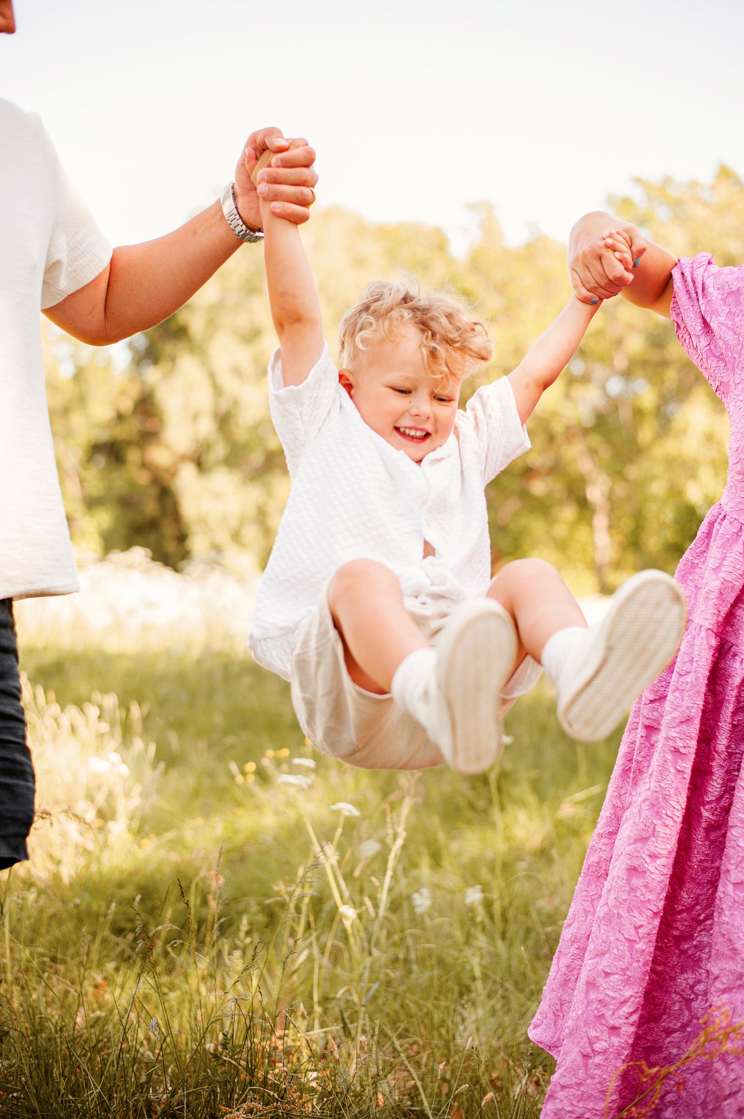 Familjefotografering i Jönköping. Pojke på 3 år busar med sin föräldrar i en vit skjorta. Sommaräng och golden hour.