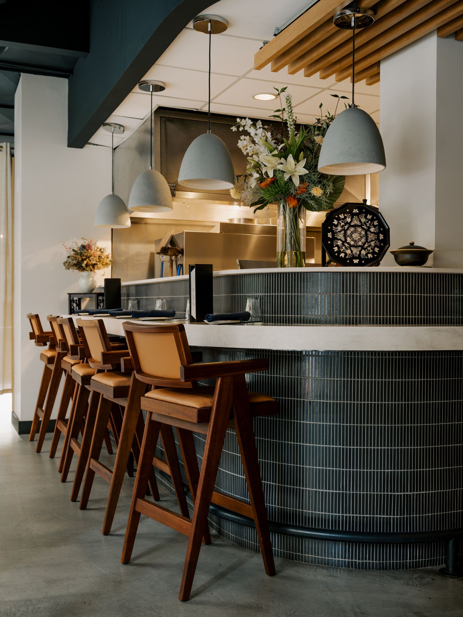 Modern restaurant bar with curved black tile base, brown leather barstools, and gray dome pendant lights above.