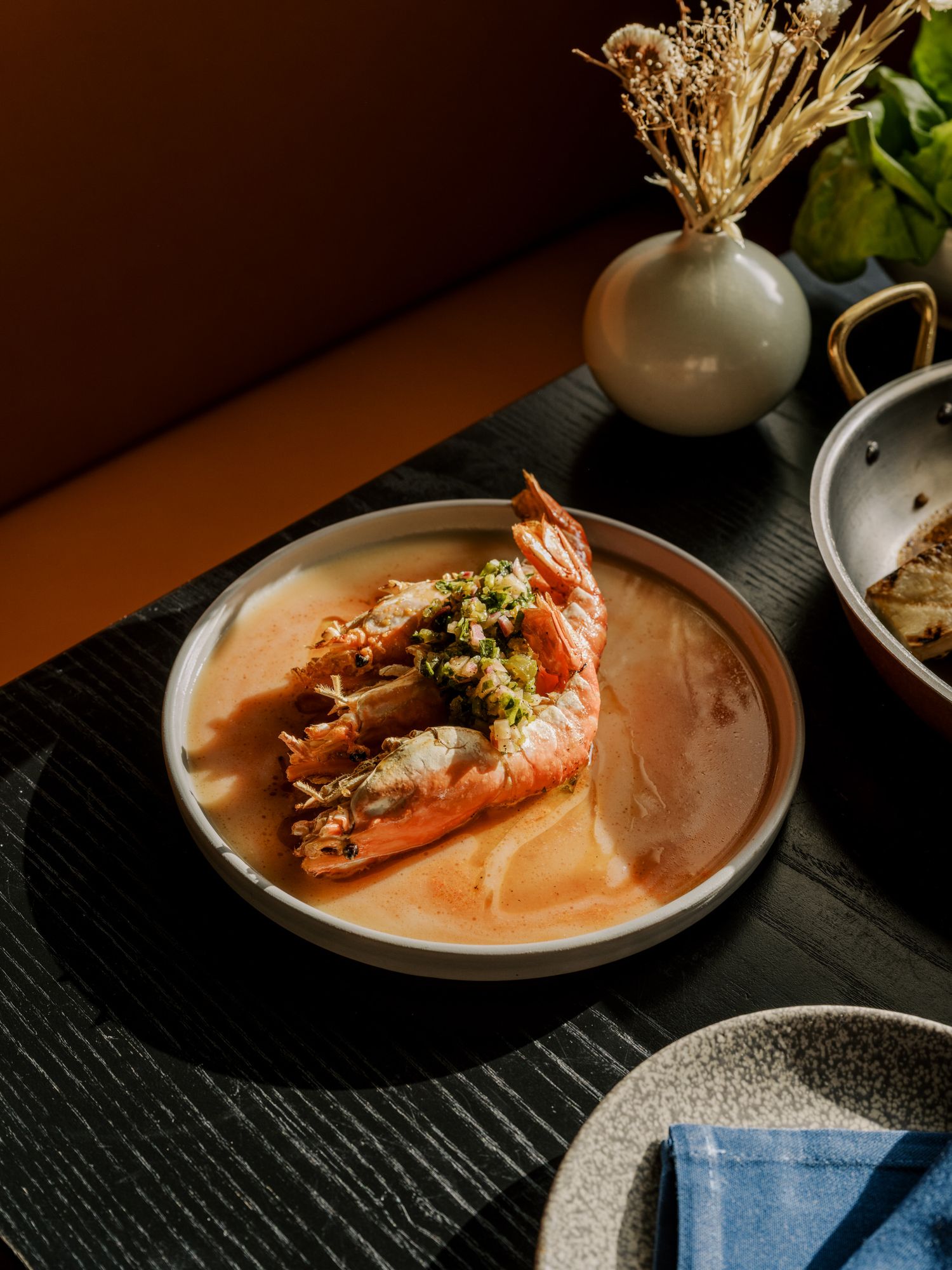 Grilled prawns served in a creamy orange-hued sauce on a ceramic plate with decorative table setting.