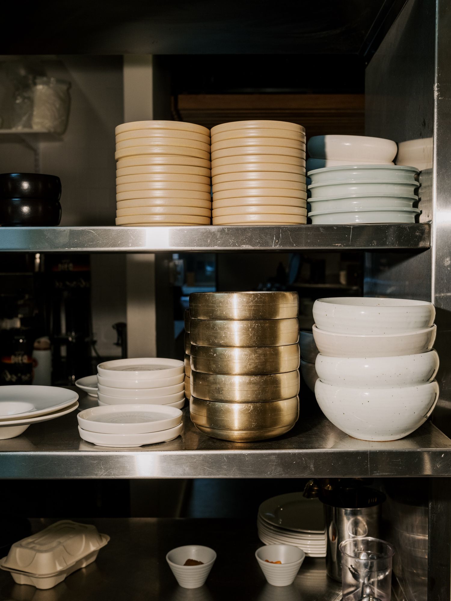 Stacks of ceramic plates and bowls organized on metal shelves in a commercial kitchen storage area.
