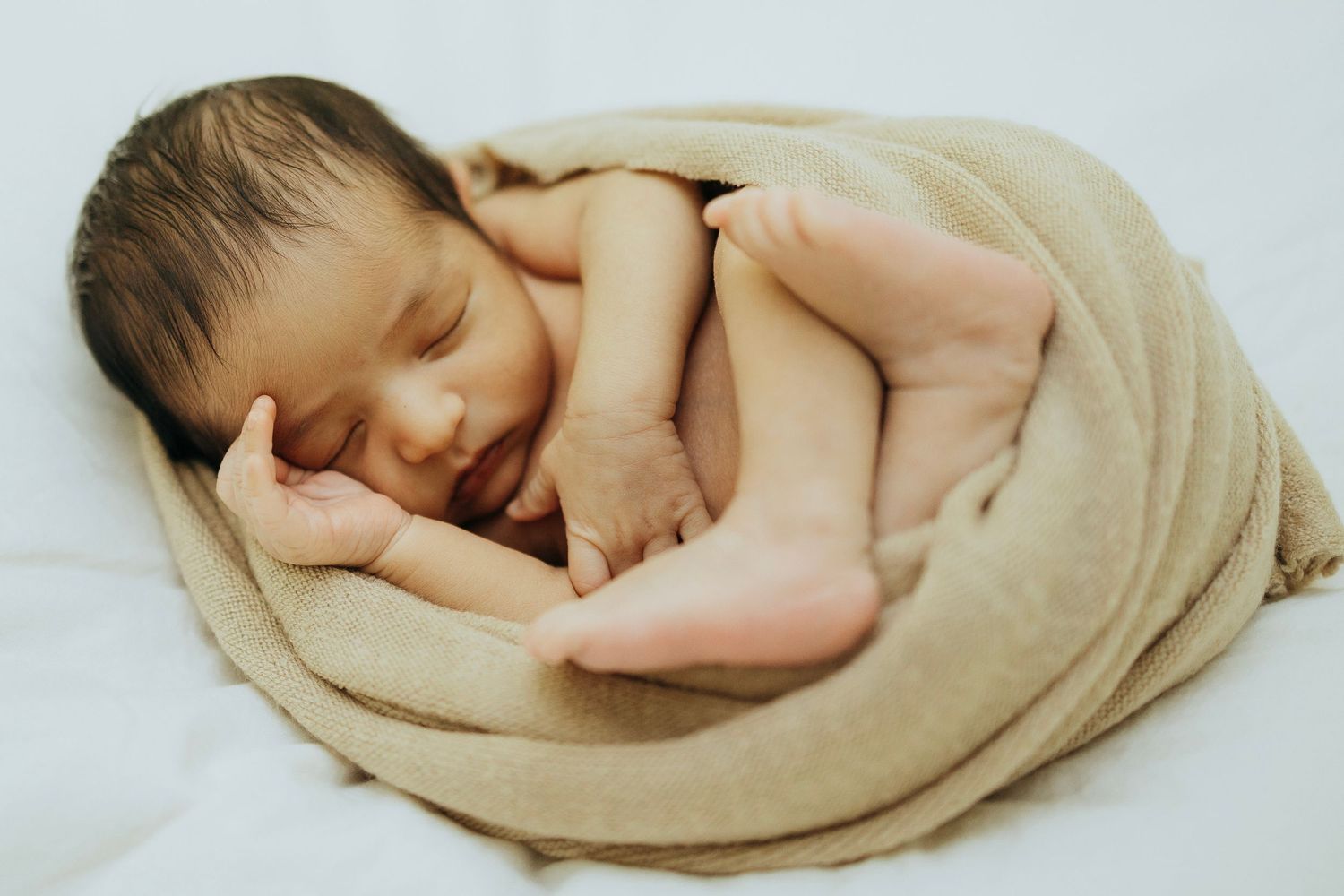 Peaceful sleeping newborn curled up in soft beige blanket.