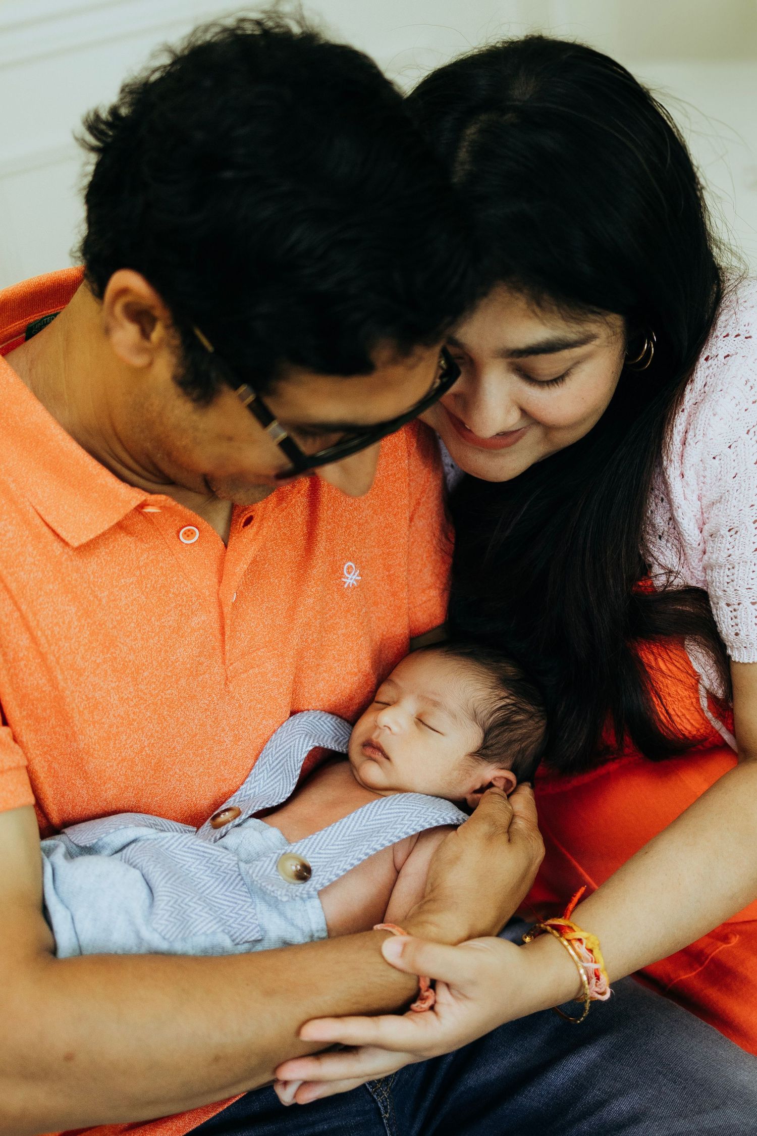 Family shares intimate moment with sleeping newborn in blue outfit.