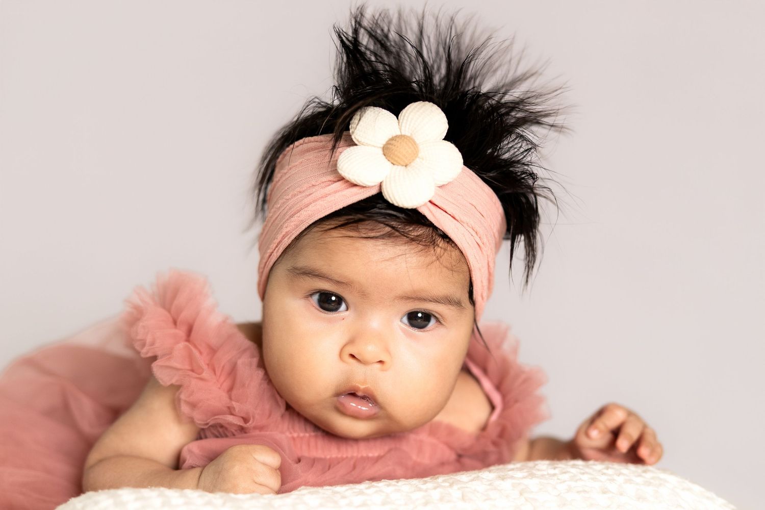 Adorable baby girl wearing a pink tutu outfit and floral headband with feathers, posed for a professional portrait photo.