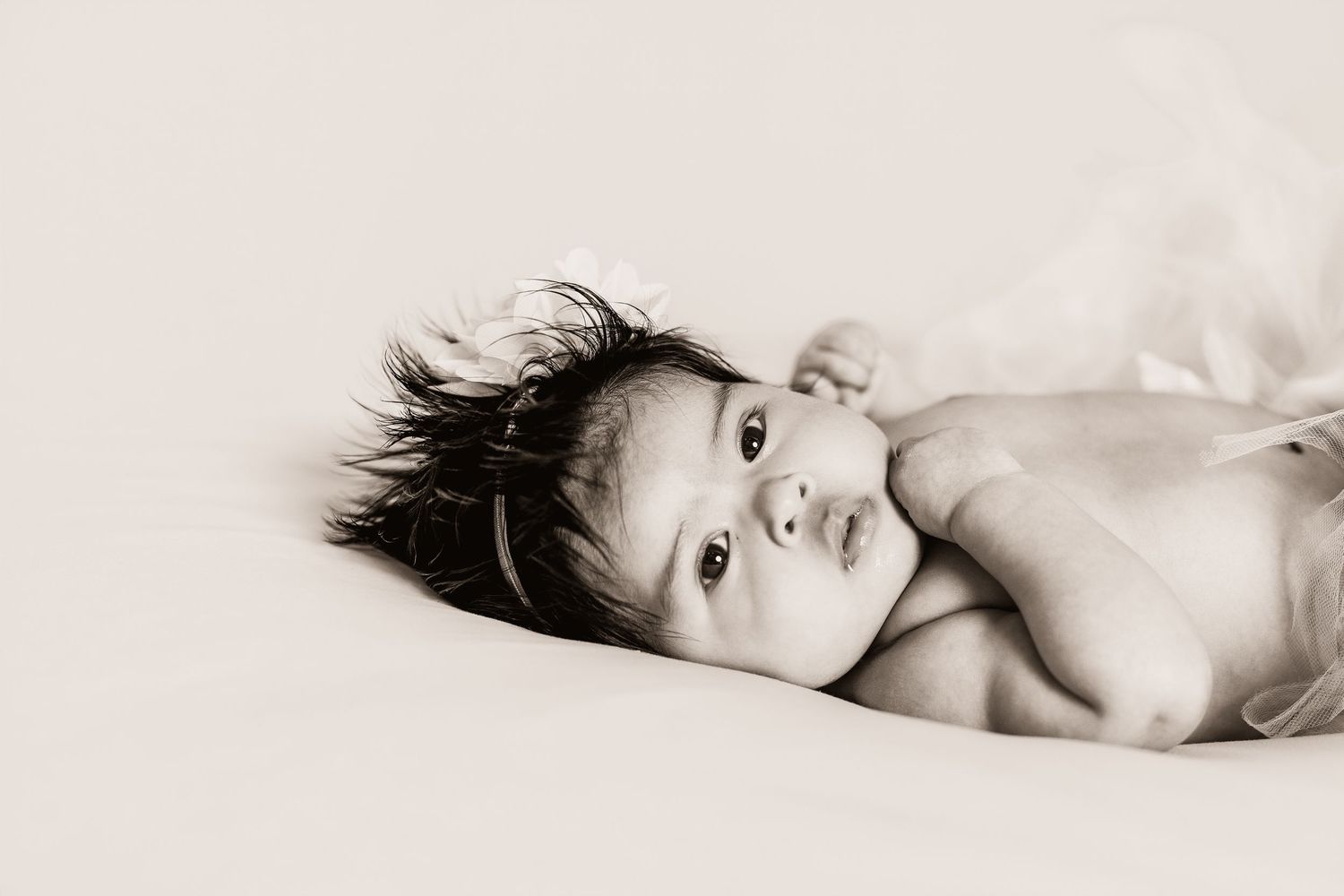 Black and white newborn baby portrait lying on soft blanket with dark wispy hair and bright curious eyes.