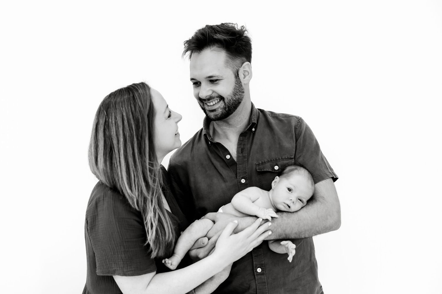 Black and white photo of smiling parents holding their newborn baby against a white background.
