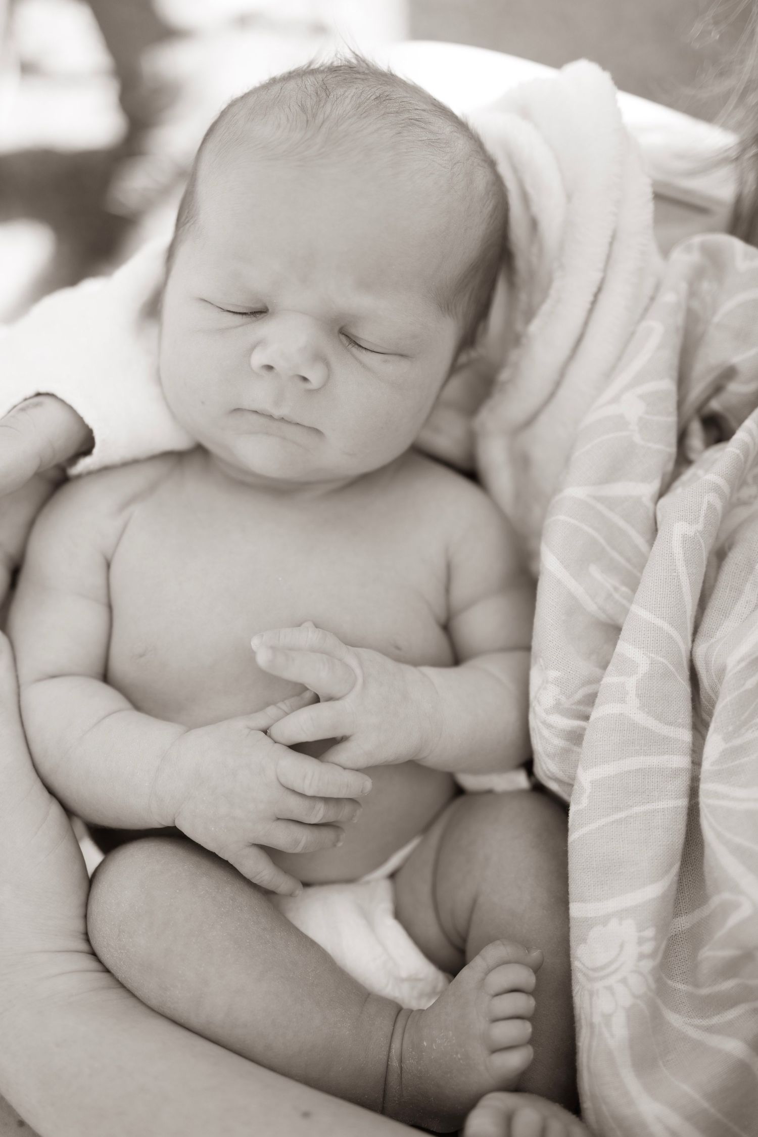 Peaceful sleeping newborn baby swaddled in white blankets in black and white portrait.