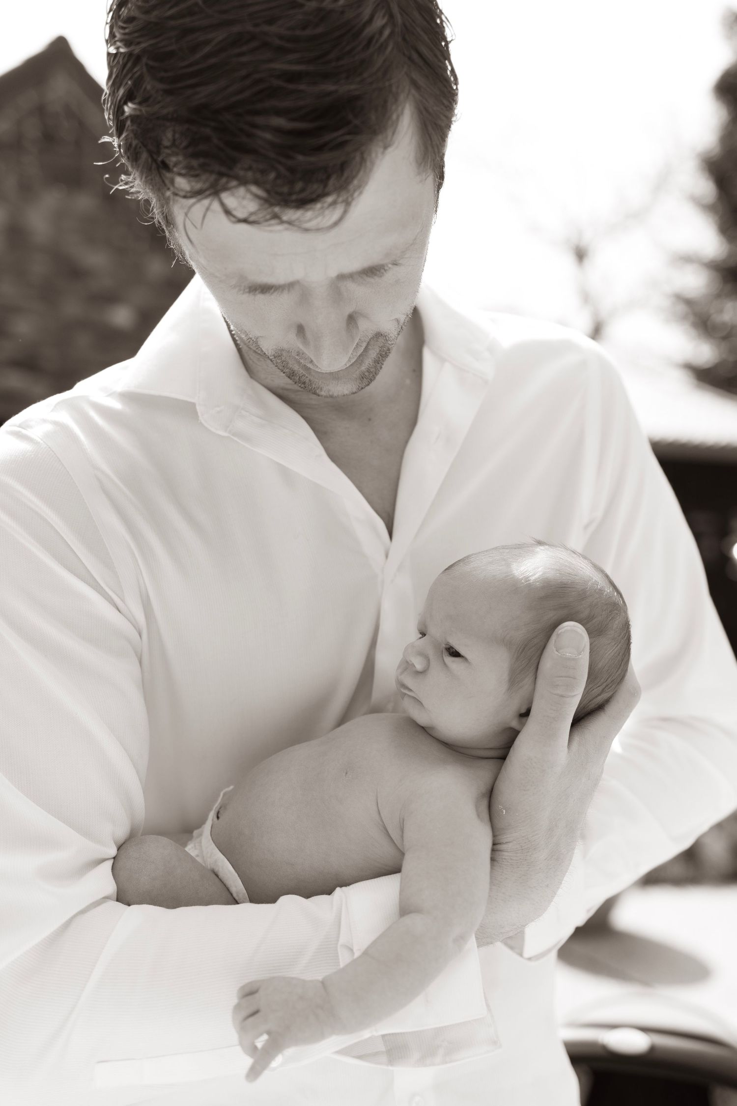 Artistic black and white series of parent cradling newborn in white shirt.