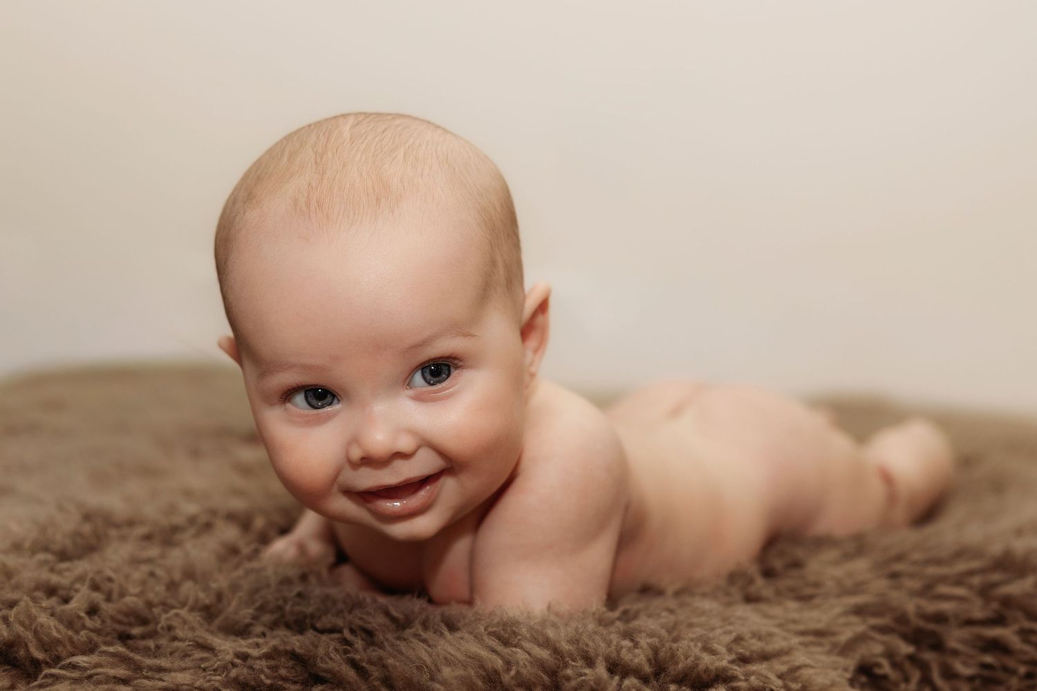 Smiling baby lying on fluffy brown rug, tummy time portrait photo.
