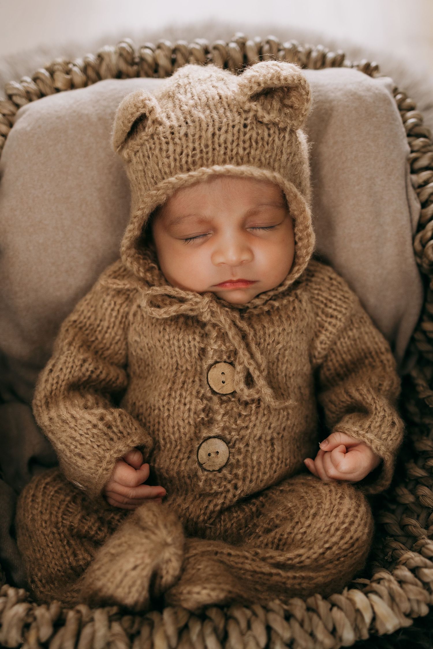 Baby wearing cozy brown knit sweater and hat sleeping on plush cushion.