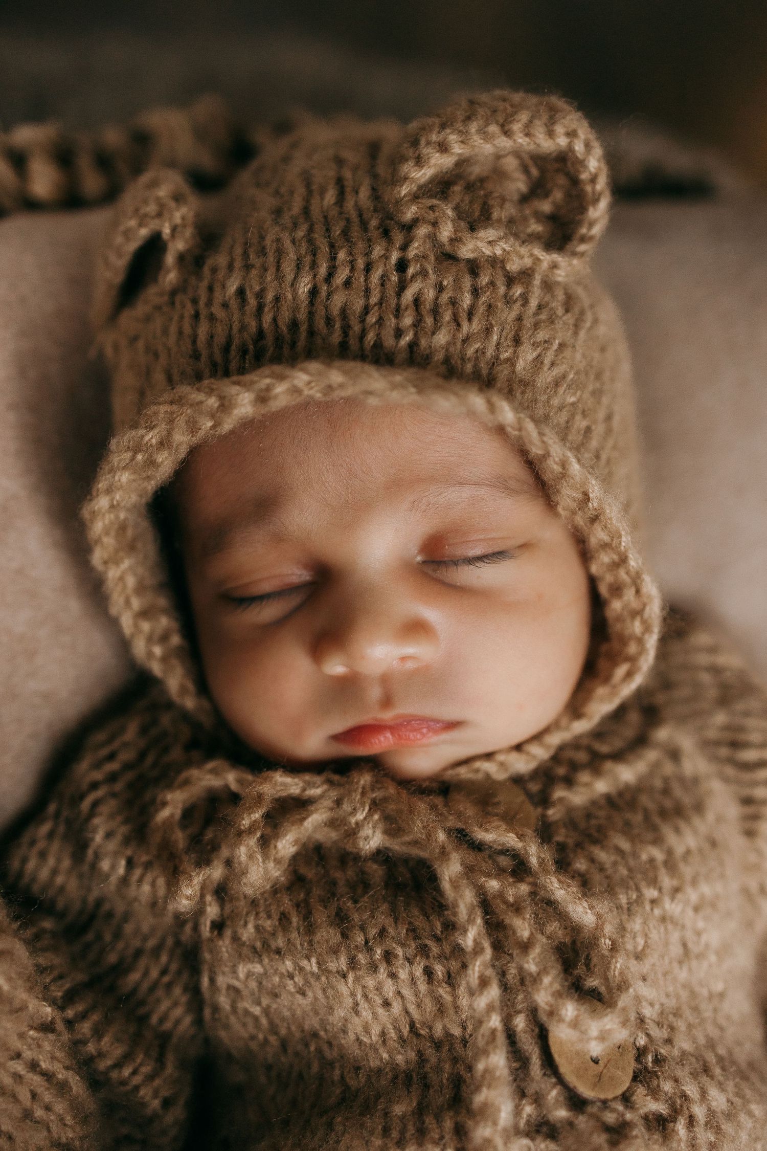 Close-up of sleeping baby in brown knitted outfit with button details.