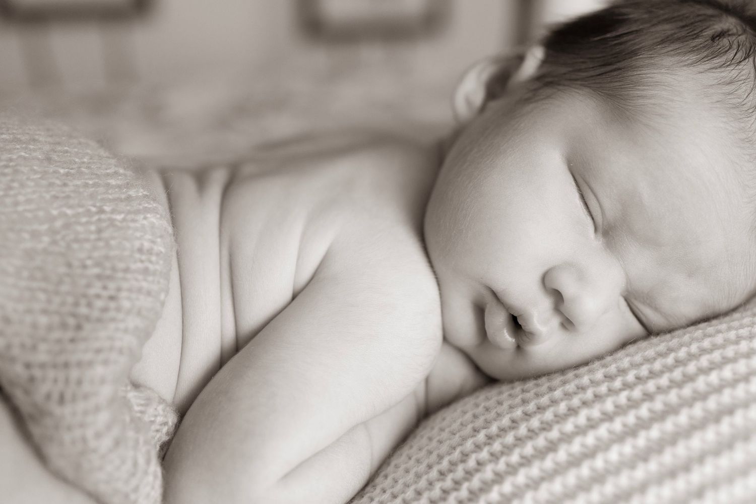 Sleeping infant wrapped in soft textured blankets in monochrome.