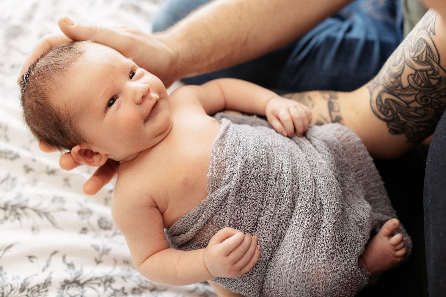 Newborn baby wearing gray knit sweater resting on textured bedding.