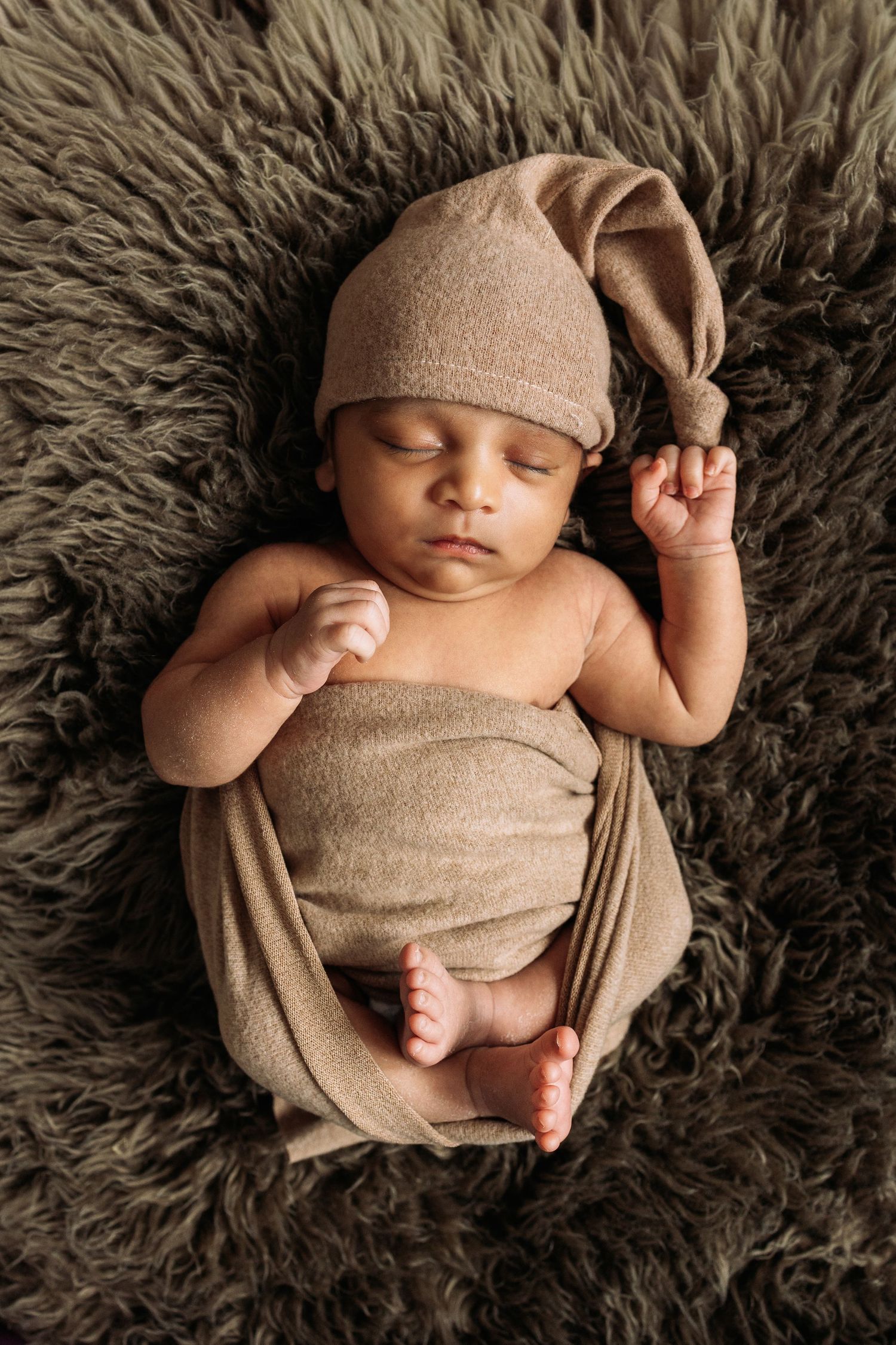 Sleeping newborn in beige outfit lying on gray furry blanket.