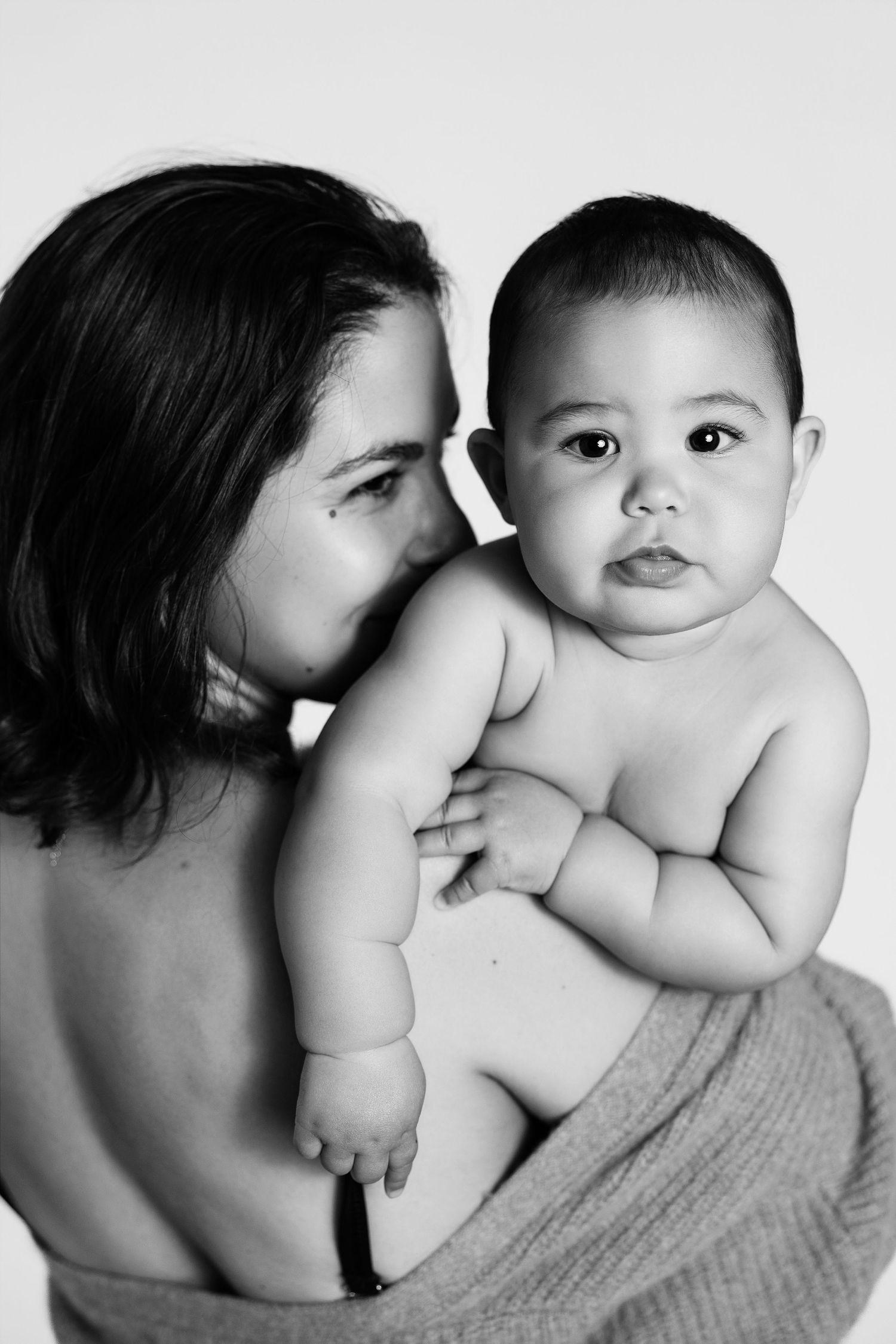 Black and white photo of a mother kissing her chubby baby on a white background.