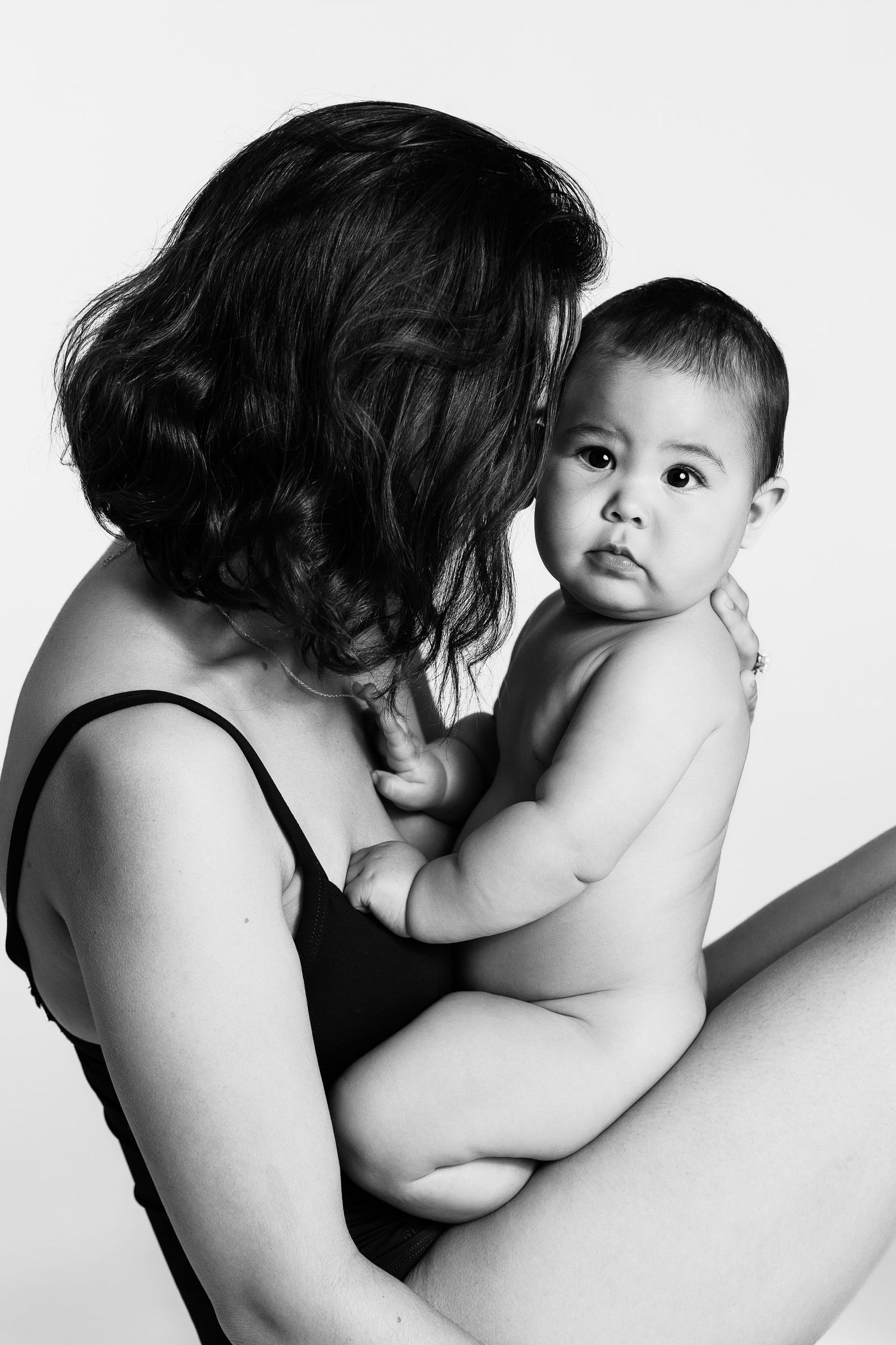 Black and white photo of a mother tenderly holding her chubby baby, both sharing an intimate moment.