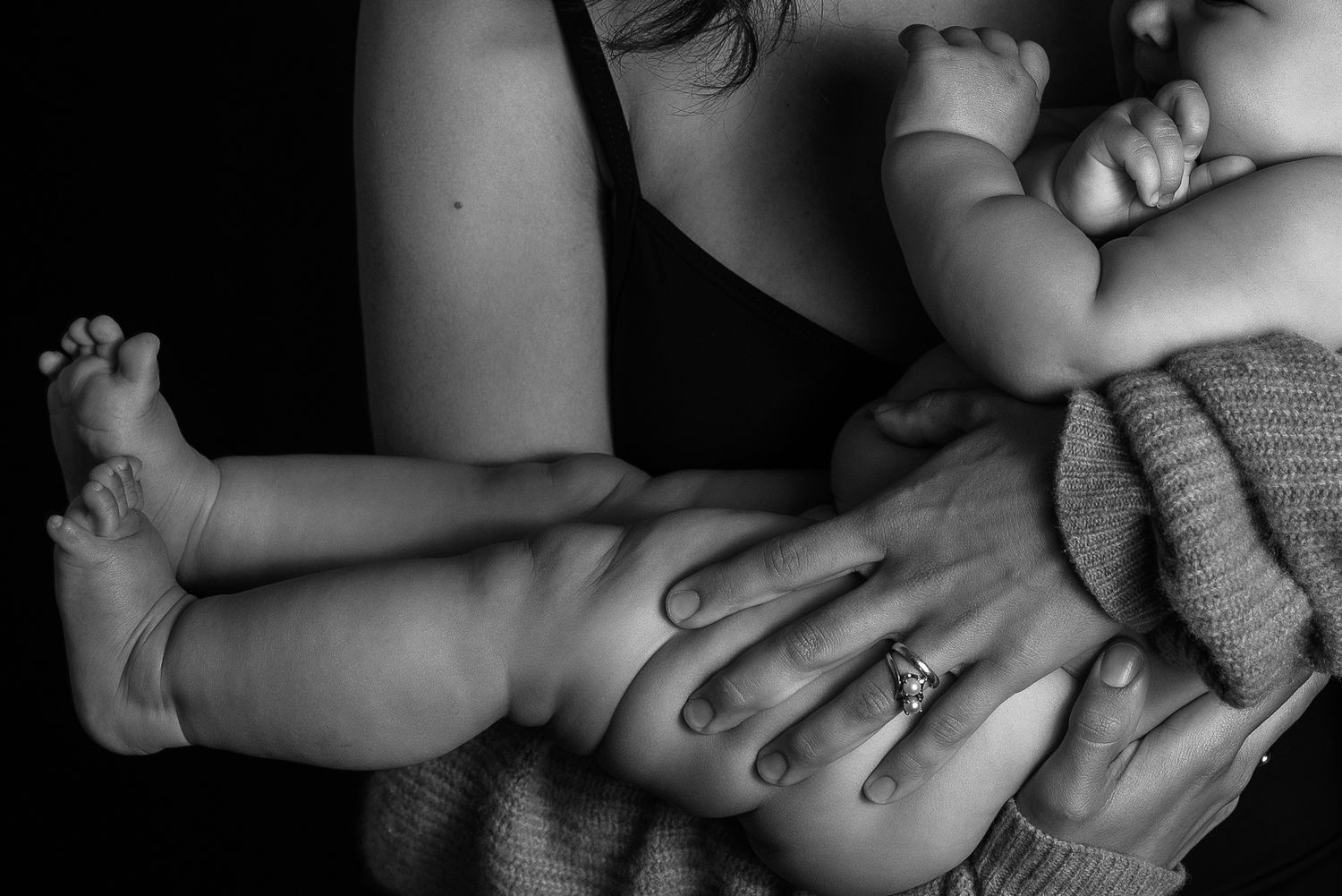 Black and white photo of a mother cradling two babies in her arms, wearing a ring on her finger.